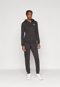 Μαύρο φούτερ με φερμουάρ και κουκούλα με κορδόνι, με γκρίζο λογότυπο, σε συνδυασμό με τζόγκερ που ταιριάζουν. Και τα δύο έχουν ριμπ μανσέτες και απαλή υφή.