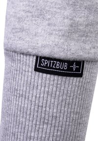 Grau gestrickte Socke mit geripptem Muster, versehen mit einem schwarzen Etikett mit dem Text und Logo "SPITZBUB" in der Nähe des Bündchens. Weiches und dehnbares Material.