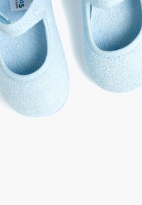Zapatos de tela azul claro con una superficie texturizada y punta redondeada. Presentan un diseño troquelado y una correa elástica para un ajuste seguro.