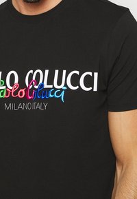 Camiseta negra de algodón con texto bordado colorido: "Pablo Colucci Milano Italia" en diferentes colores vibrantes sobre la tela negra.