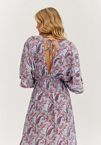 Kvetinové šaty s paisley vzorom na svetlomodrom základe, s gumičkovaným pásom, širokými rukávmi a otvoreným chrbtom viazaným mašľou.