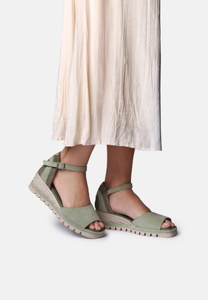 Voeten met saliegroene sleehakken met enkelbandjes en open tenen, gecombineerd met een luchtige off-white rok.