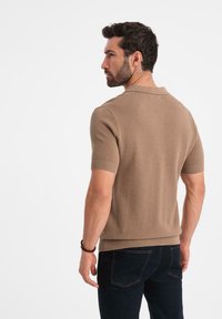 Polo de manga corta en tono claro, confeccionado en tejido de punto texturizado y con puños acanalados. Combinado con jeans oscuros, mostrando un diseño ajustado.