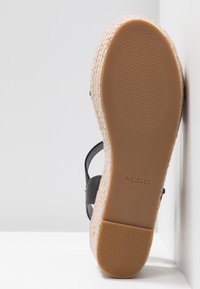 Sandale noire avec une semelle en jute tressé, dotée d'un coussin en caoutchouc lisse et d'une surface inférieure texturée pour une meilleure adhérence. La marque est présente sur la semelle.