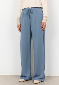 Pantaloni azzurri chiari a gamba larga realizzati in un tessuto morbido, con vita elastica e cordoncino. Indossati con una maglietta beige a maniche lunghe e scarpe neutre.