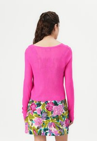Maglione aderente a maniche lunghe di colore rosa a coste con scollatura ampia, abbinato a una gonna con stampa floreale caratterizzata da vivaci tonalità di rosa, verde e blu.