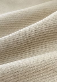 Tessuto beige con una fine trama a coste che mostra pieghe e ombre delicate.