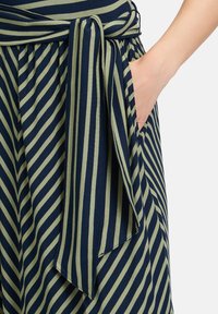 Sukienka z zielono-granatowym paskowanym materiałem, z wiązanym pasem w talii, pionowymi paskami i otwartą kieszenią po lewej stronie.