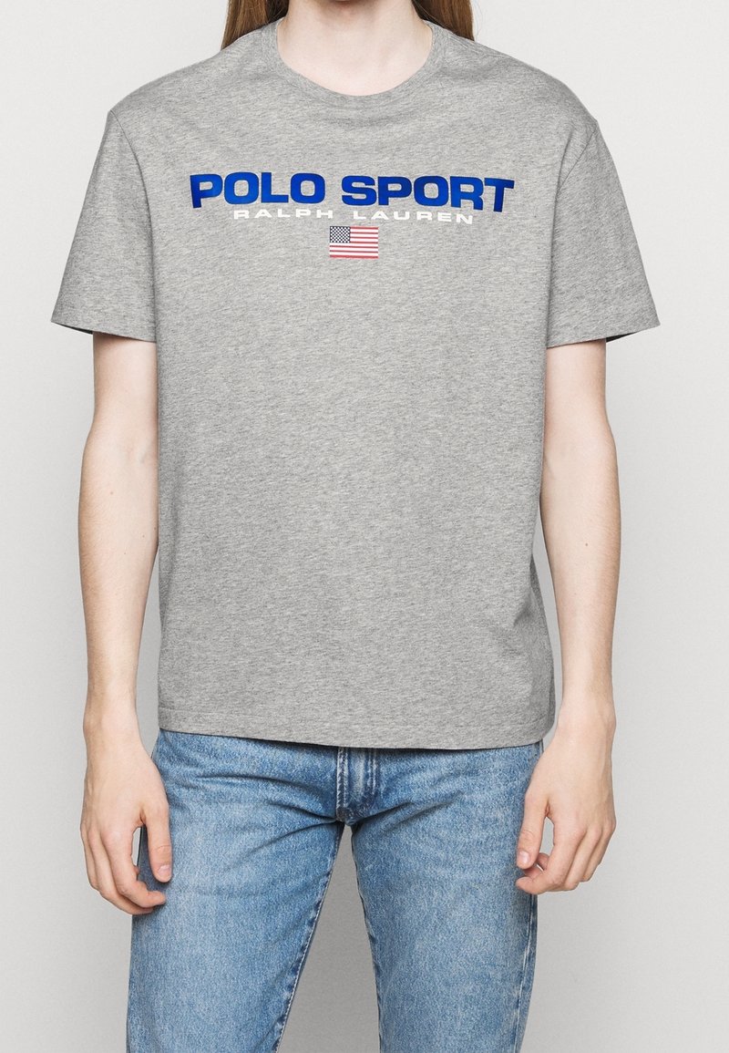Šedé bavlněné tričko s kulatým výstřihem, krátkými rukávy a výrazným modrým nápisem „POLO SPORT“ doplněným malým motivem americké vlajky.