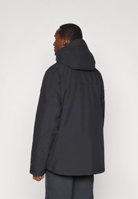 Μαύρο φούτερ μπουφάν με λεία υφή, ελαφρώς χαλαρή εφαρμογή και οριζόντια ραφή πίσω για επιπλέον λεπτομέρεια σχεδίασης.