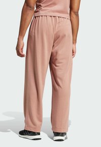 Lyserøde, afslappede sweatpants lavet af blødt stof med brede ben og elastisk talje, parret med sorte løbesko.