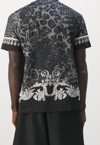 Kortärmad svart t-shirt med ett leopardskinnsmotiv och dekorativa blommönster i grått vid fållen och ärmarna.