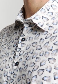 Korte mouwen overhemd met een lichtgrijze basis en een patroon van blauwe en zwarte oesterschelpen illustraties. Voorzien van een knoopkraag en donkere knopen.
