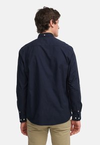 Chemise à manches longues bleu marine avec col à boutonnière et manches à poignets. Fabriquée dans un tissu doux, elle présente un ourlet inférieur droit et de subtils détails de couture.