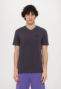 Dark gray v-neck t-shirt made of soft cotton, featuring short sleeves and a small black logo on the chest. Simple, minimalist design.