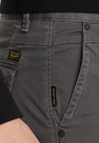 Graue Baumwollhose mit glatter Textur, mit dezentem Stich, abgerundeten Fronttaschen und Markentags in Schwarz und Gelb.