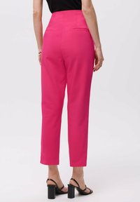 Hoge taille roze broek met een taps toelopende pijp, voorzien van achterzakken en een gladde textuur, gecombineerd met zwarte sandalen op blokhak.