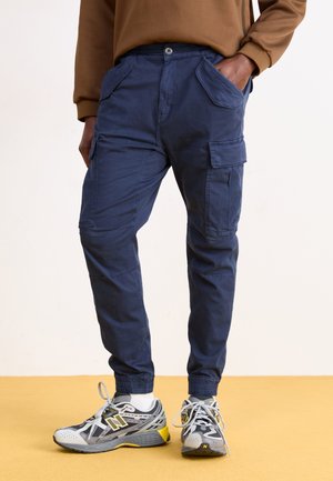 Pantalones cargo azul marino con puños elásticos, bolsillos frontales y bolsillos laterales, fabricados en un tejido suave y ligero. Combinados con zapatillas grises.