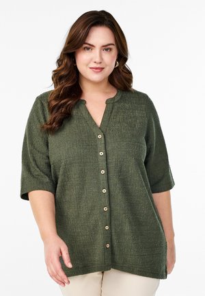 Grøn kortærmet skjorte med knapper, tekstureret mønster, rund halsudskæring og træknapper ned foran. Løs pasform, midt på hoften.
