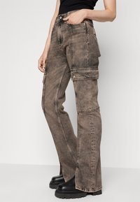 Pantalones cargo de mezclilla marrón desgastado con cintura alta, piernas anchas y bolsillos laterales. Presenta costuras prominentes y detalles de botones de metal.