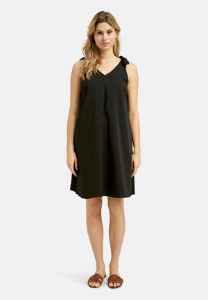 Schwarzes ärmelloses Kleid mit V-Ausschnitt und geknoteten Trägern. Fließendes, knielanges Design mit glatter Textur. Kombiniert mit braunen Sandalen.