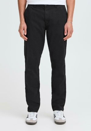 Black, straight-leg trousers made of a smooth fabric, featuring a button closure and belt loops, paired with white sneakers.