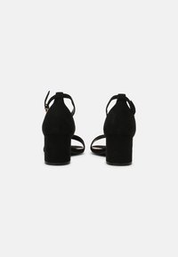 Svarta mocka klacksandaler med blockklack, öppen remdesign och ankelrem fastsättning. Slät textur, minimalistisk stil.