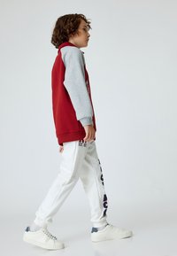 Rød og grå sweatshirt med lange ærmer og hætte, parret med hvide sweatpants med marineblå tekst. Båret med hvide sneakers.