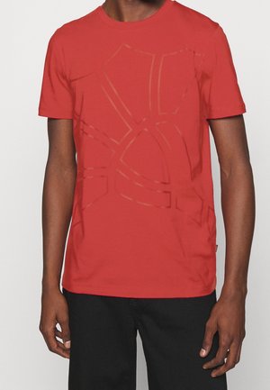 Camiseta de algodón roja con cuello redondo, que presenta un diseño gráfico en un tono ligeramente más oscuro. Mangas cortas y un ajuste relajado.