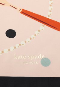 Rosa stof med et guld logo "kate spade NEW YORK," samt en illustration af en rød ske og hvide perler på en sort og mintgrøn baggrund.