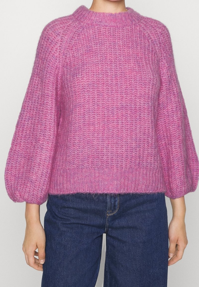 Pull-over en tricot dans différentes nuances de rose, avec un col rond, des manches bouffantes et un ourlet côtelé, présentant une finition douce et texturée.
