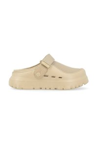Zapatilla tipo zueco color beige con parte superior texturizada, correa ajustable, suela gruesa y orificios de ventilación a lo largo del costado. Material ligero.