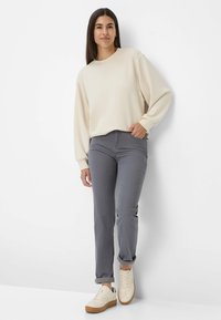 Sweatshirt beige à manches longues, associé à un pantalon gris slim et des sneakers blanches avec une semelle beige. La tenue a une coupe décontractée.