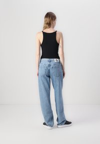Black sleeveless top, light blue oversized jeans, and black sneakers. Jeans feature a label on the back waistband and two rear pockets.