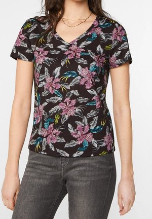 Kobieta w czarnej koszulce z krótkim rękawem i dekoltem w serek z różowo-niebieskim kwiatowym wzorem, w zestawieniu z ciemnoszarymi dżinsami i cienkim złotym naszyjnikiem.