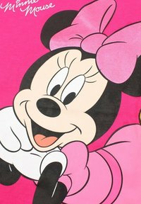 Graphisme de Minnie Mouse sur un fond rose, mettant en avant un personnage souriant avec un grand nœud, des oreilles noires et des gants blancs.