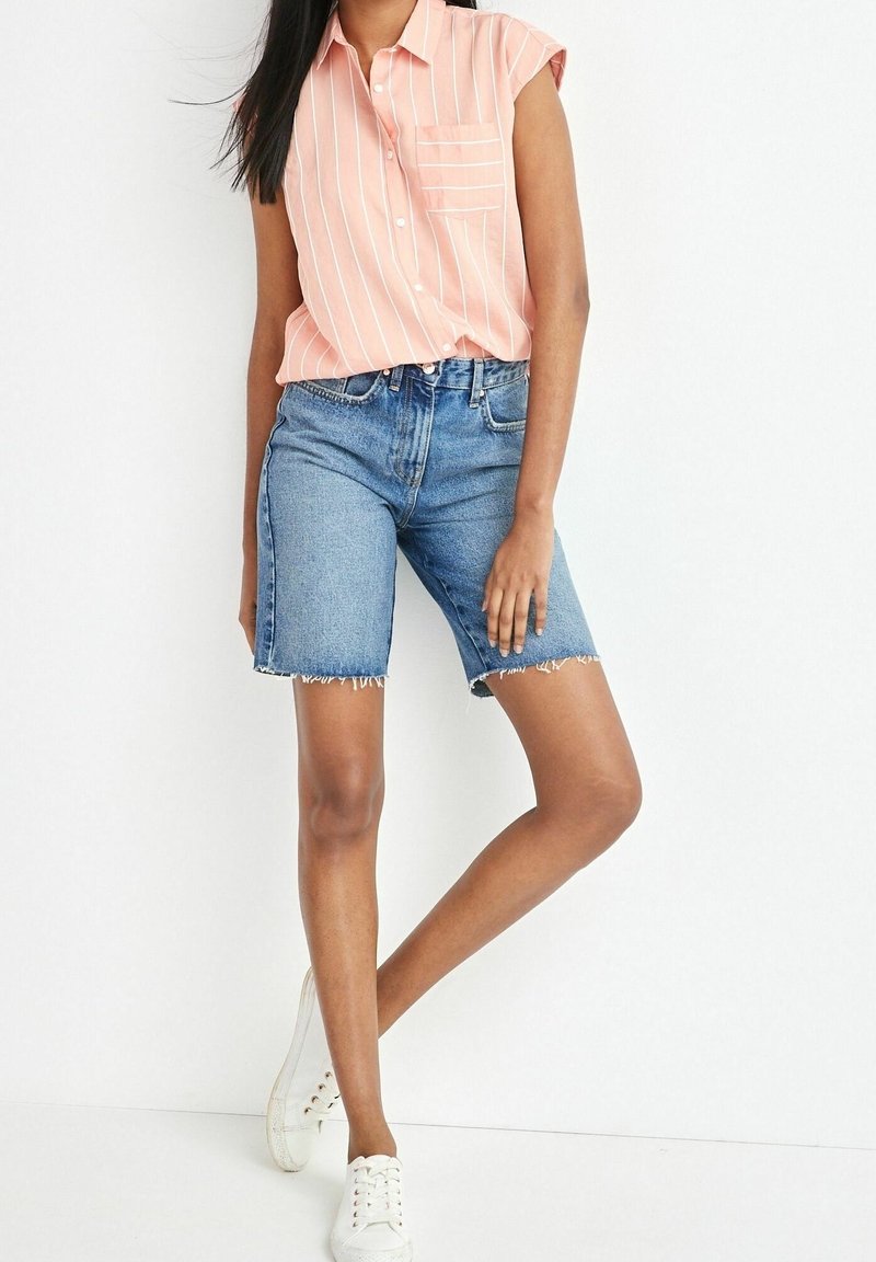 Camiseta sin mangas de color rosa claro con rayas blancas y bolsillo frontal; combinada con pantalones cortos de mezclilla azul de cintura alta con dobladillo deshilachado. Zapatillas blancas.