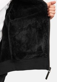 Chaqueta negra forrada de felpa con una textura exterior suave, cierre frontal con cremallera y dobladillo acanalado. El interior cuenta con una tela suave y mullida para mayor calidez.