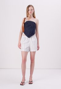 Top en denim sans manches avec un ourlet pointu, associé à un short à rayures blanches et marines. Le mannequin porte un sac à épaule en faux cuir marron.