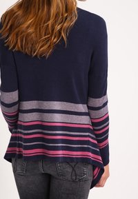 Námořnický svetr s vodorovnými pruhy v světle šedé, růžové a tmavě růžové barvě. Měkká pletenina, volný střih a delší zadní lem.