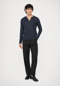 Tamsiai mėlynas ilgomis rankovėmis henley marškinėliai su gobtuvu, turintys sagčių apykaklę. Derinama su juodais pritaikytais kelnėmis ir juodomis avalynėmis. Paprastas dizainas.