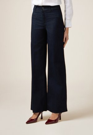 Szerokie ciemnoniebieskie jeansy o wysokim stanie, z przednimi kieszeniami i gładką teksturą, w połączeniu z burgundowymi butami na wysokim obcasie.