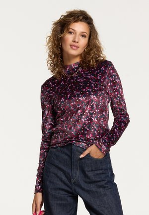 Langere mouwen, neklijst top in donkerpaarse fluweel met een bloemenpatroon in roze, wit en groen. Gecombineerd met een high-waisted spijkerbroek.