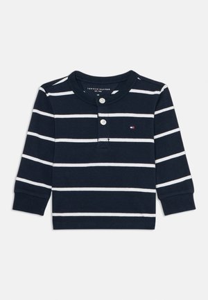 Marineblå langermet skjorte med hvite striper, rund krage, to knapper, og liten logo på brystet. Cottenmateriale, myk tekstur.
