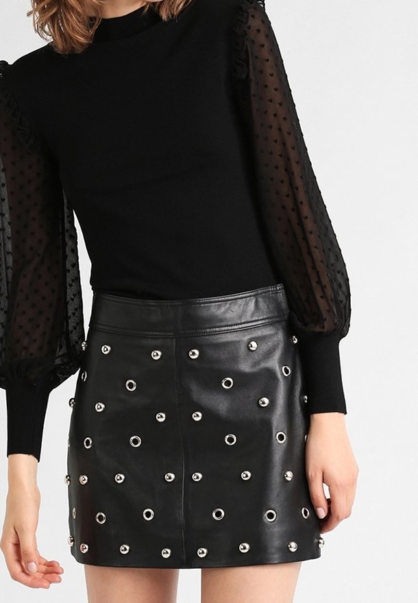 Schwarzes gestricktes Oberteil mit gerafften, transparenten Tupfenärmeln, kombiniert mit einem schwarzen Lederminirock mit silbernen Ösen-Details und figurbetontem Schnitt.