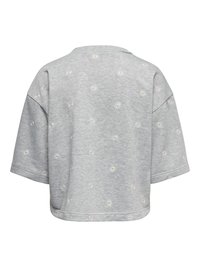 Svetlo siva oversized majica z širokimi rokavi, okrašena z malimi belimi in rumenimi vezenimi marjeticami, razporejenimi po tkanini.