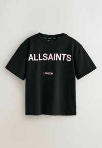 Melna kokvilnas T-kreklā ar drosmīgu rozā krāsu "ALLSAINTS" tekstu uz krūtīm un "LONDONA" zem tā, ar klasisku apaļu kakla izgriezumu un īsām piedurknēm.