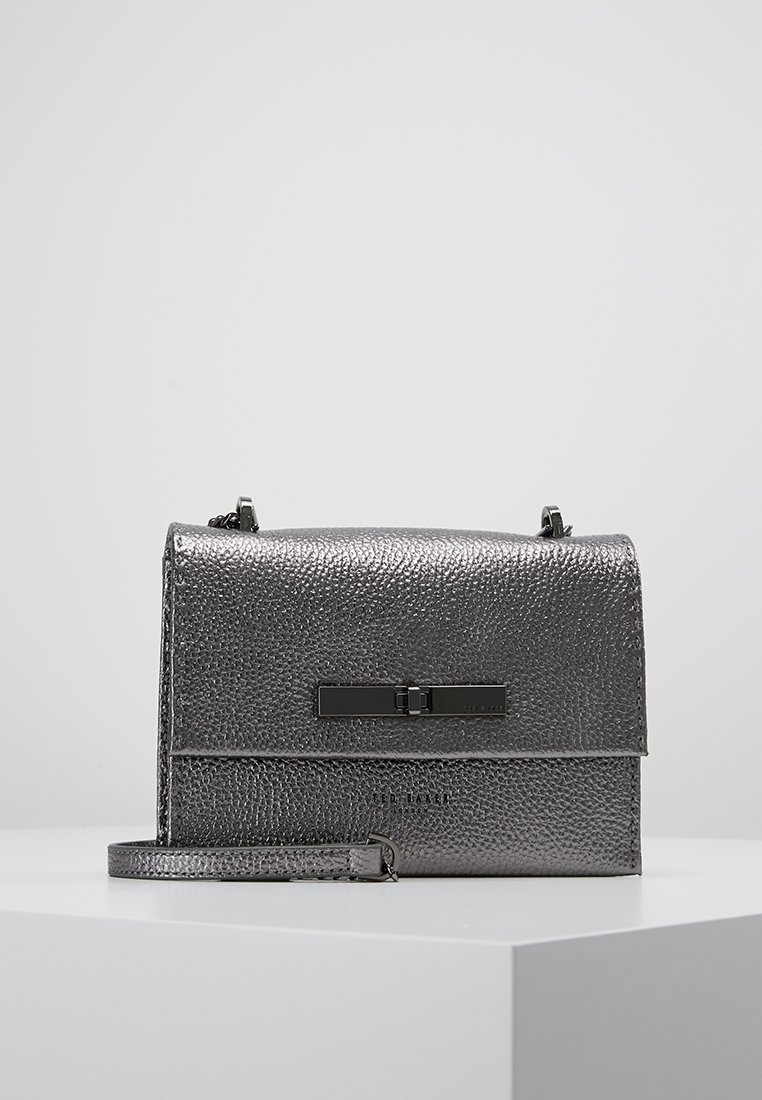 Szara torebka ze skóry o fakturze, z klapą i czarnymi metalowymi elementami oraz odpinanym paskiem. Konstrukcja o pudełkowatym kształcie.
