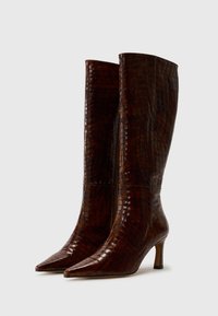 Bottes marron à hauteur de genou avec un bout pointu, un motif texturé en crocodile et un talon fin. Fabriquées en matériau brillant avec une finition lisse.