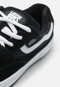 Black suede sneaker with white mesh accents, featuring a black logo patch, white laces, and a textured white sole.